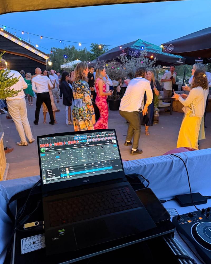 Uitzicht vanachter de DJ-set op de dansende gasten in de schemering